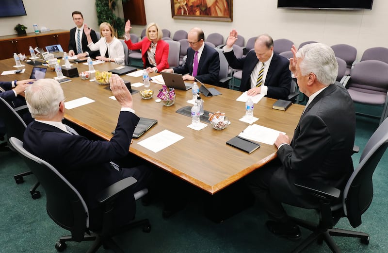 Cinco miembros del Consejo Ejecutivo de Misiones se sientan a una mesa y levantan sus manos en apoyo de un asunto durante una reunión del Consejo Ejecutivo de Misiones en el Edificio de Oficinas de la Iglesia en Salt Lake City el miércoles 26 de mayo de 2021.