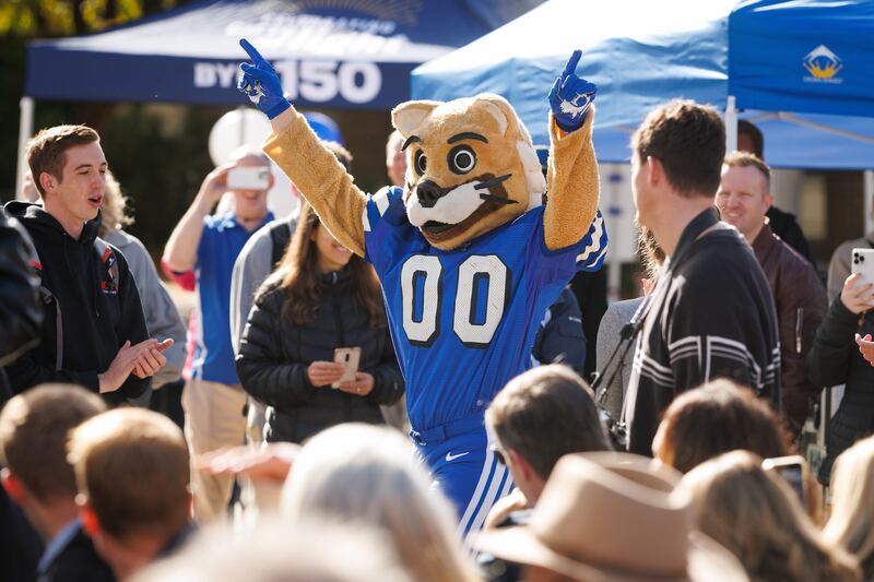 Durante un evento del Día del Fundador el 16 de octubre de 2025, la mascota de BYU, Cosmo, hace una aparición vistiendo su traje de los años 70 mientras los líderes universitarios abren una cápsula del tiempo de las celebraciones del centenario de la universidad en 1975.