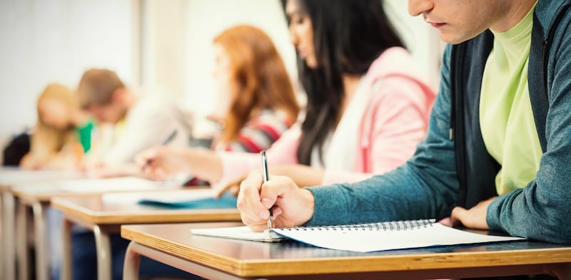 Los estudiantes se sientan en una fila de escritorios, escribiendo en cuadernos.