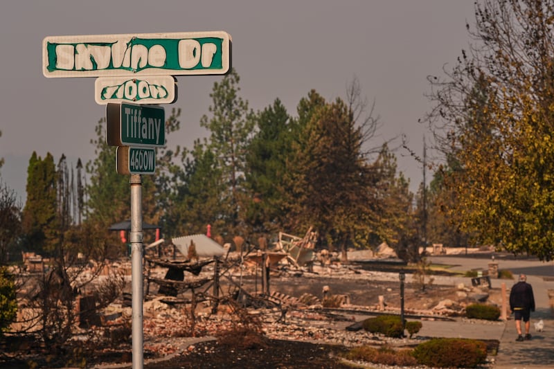 Un letrero de la calle muestra signos de daño por fuego mientras una persona pasea a su perro después de que un incendio forestal azotara la parte norte de Spokane, Washington, el lunes 3 de agosto de 2026.