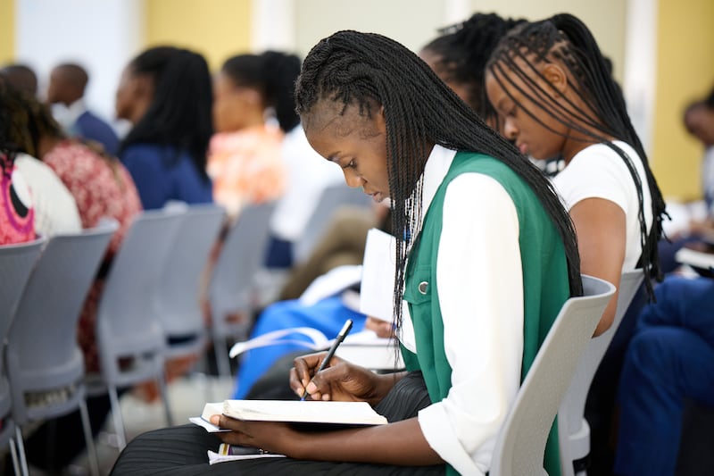 Una hermana misionera en el Centro de Capacitación Misional de la República Democrática del Congo toma notas durante un devocional con el Élder Ronald A. Rasband del Cuórum de los Doce Apóstoles el domingo 2 de noviembre de 2025.