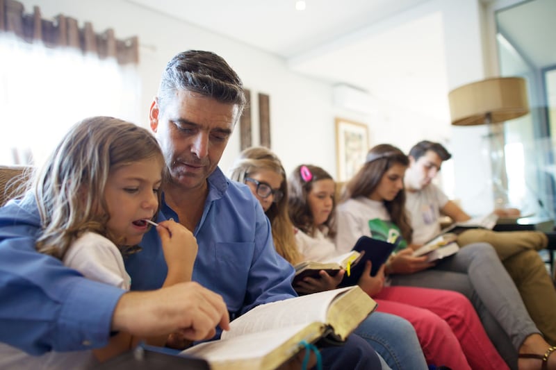 Un padre se sienta con sus hijos en su sala de estar para leer las escrituras juntos en Portugal.