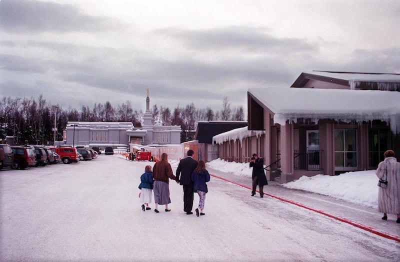 Con el Templo de Anchorage, Alaska de fondo y la casa de reuniones adyacente a la derecha, una familia es fotografiada llegando a la dedicación del templo el 9 de enero de 1999 en Anchorage, Alaska.