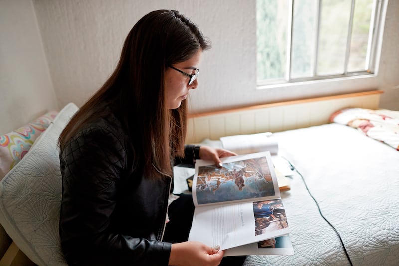 Una mujer se sienta en una cama mientras estudia el manual "Venid, seguidme".