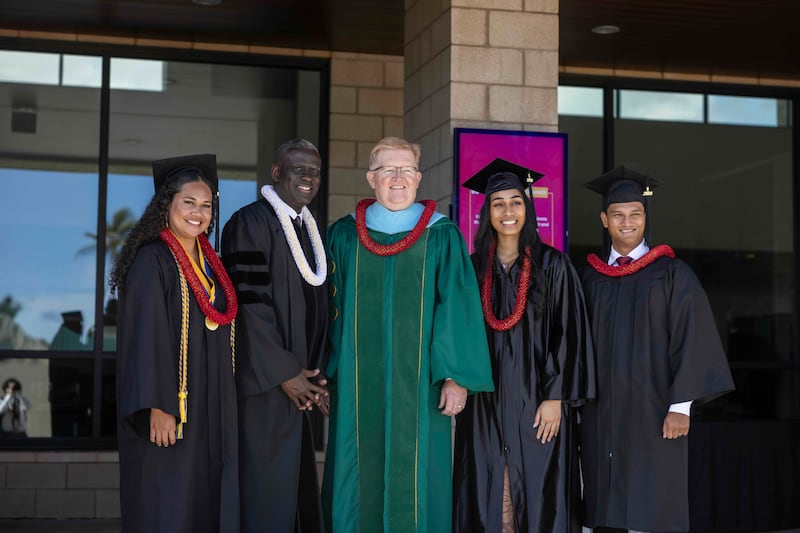 El élder Peter M. Johnson, Setenta Autoridad General, segundo desde la izquierda, y el presidente interino de BYU–Hawái, R. Kelly Haws, al centro, posan para una foto con los graduados el viernes, 17 de abril de 2026.