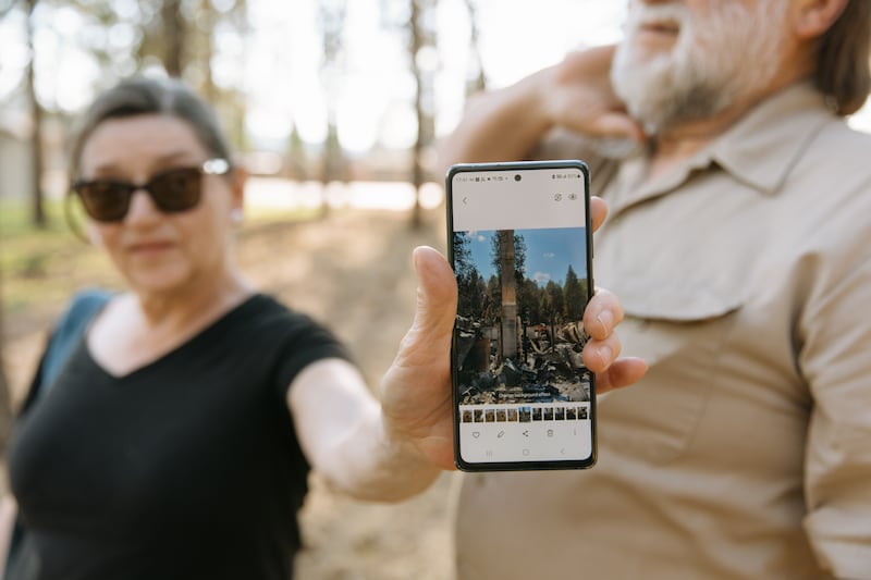Cherie Tolman sostiene una fotografía que muestra lo que queda de su hogar después de que fue destruido en los incendios forestales de Spokane a principios de agosto en Spokane, Washington, el sábado 22 de agosto de 2026.