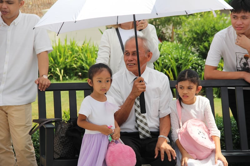 Un abuelo se sienta bajo una sombrilla con dos niñas en los terrenos del Templo de Davao, Filipinas, el último día de la casa abierta al público, el 10 de abril de 2026.