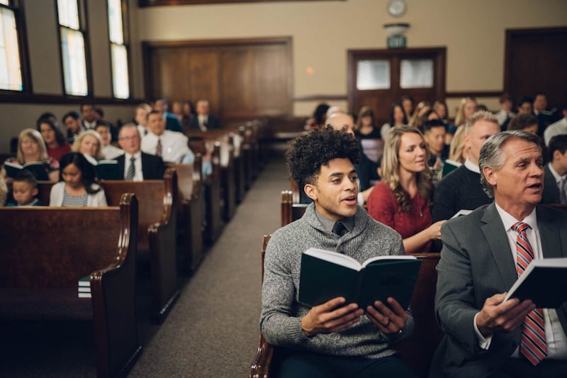 Las personas se sientan en los bancos de la iglesia y cantan como congregación.