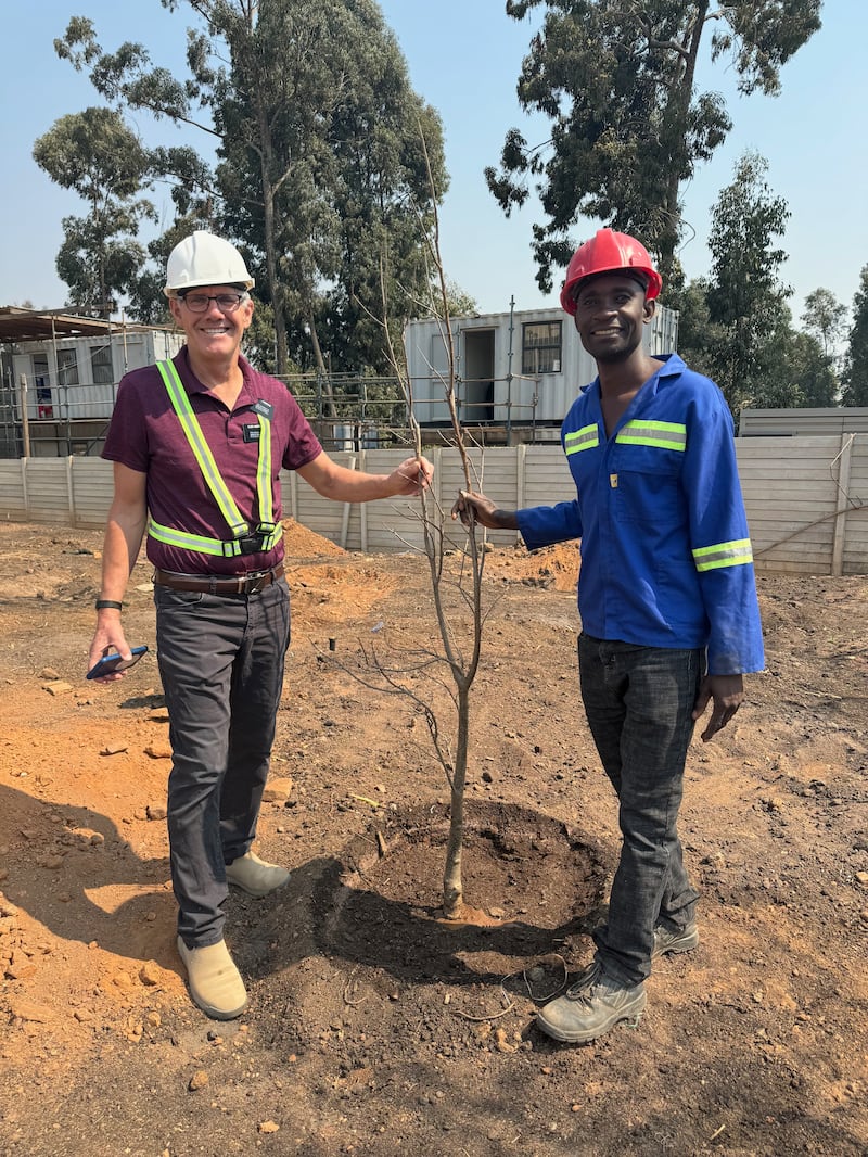 El élder Bruce Anderson y Kilford Shereni están junto a un árbol joven en los terrenos del Templo de Harare, Zimbabue.
