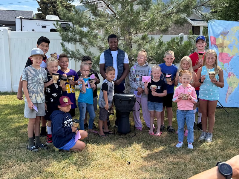 Los niños de la Primaria del Barrio Cherry Lane, Estaca Layton Utah Este, aprenden a tocar un tambor africano en un campamento de verano de historia familiar.